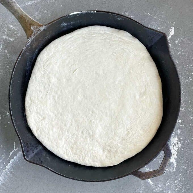 The rolled out dough to make the base of the pizza pressed into a deep skillet frypan.