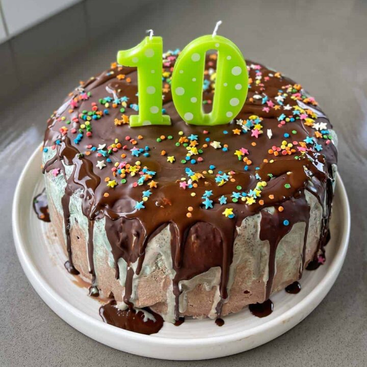 An ice cream cake with green '10' candles on it on a grey bench.