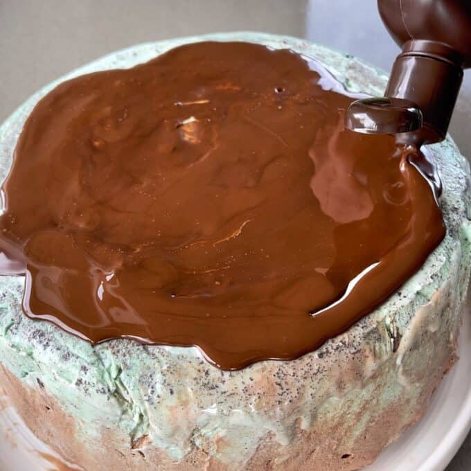 An ice cream cake with chocolate topping being poured over the top.