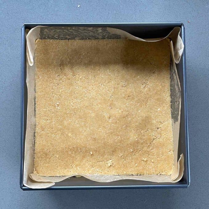 The base of a cheesecake slice sitting in a lined baking tin.