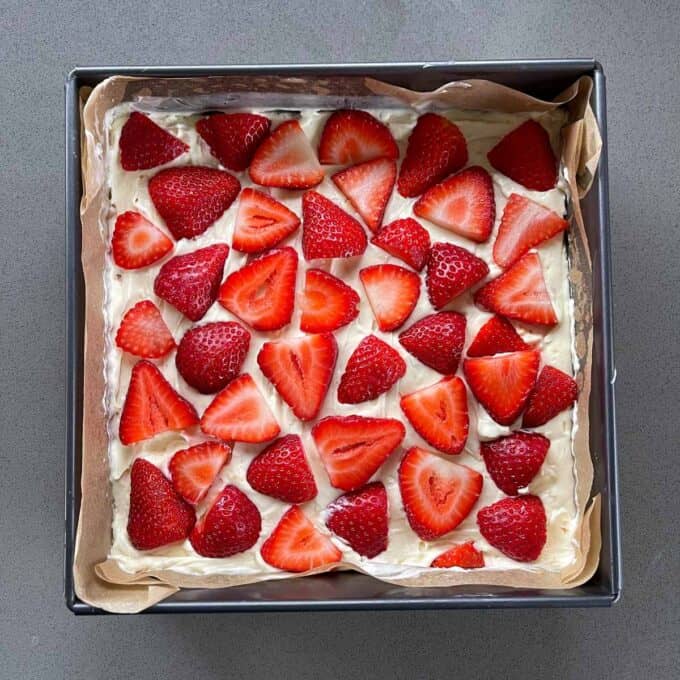 Sliced strawberries on top of a cheesecake slice on a grey bench.