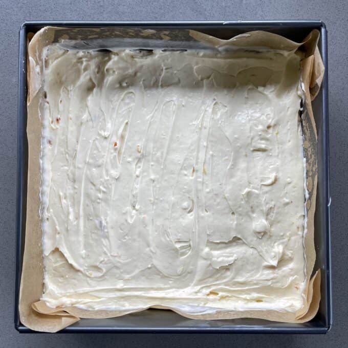 Cheesecake filling spread over a cookie base in a lined baking tin.