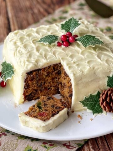 A close up of two slices of Christmas cake with the corner removed showing the fruit cake filling.