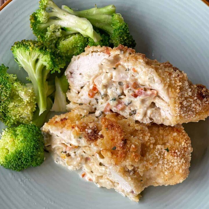 One sliced Crumbed Chicken Breast filled with sundried tomatos, basil leaves, garlic ,onion and cream cheese. Served with steamed broccolli on a duck blue dinner plate.