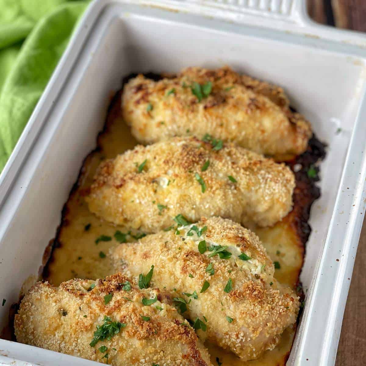 4 cooked, crumbed chicken breasts in a roasting dish.