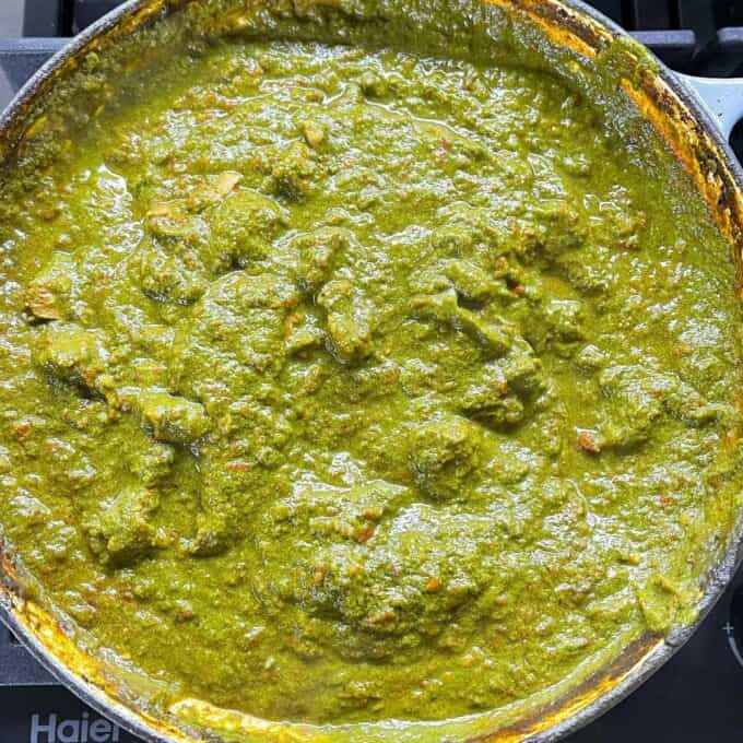 Lamb Sagg curry mixture once the blended spinach and coconut milk has been added simmering in a round ceramic dish over a medium heat.