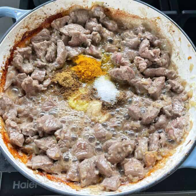 Diced lamb, garlic, onion and spices frying in a round ceramic dish over a medium heat