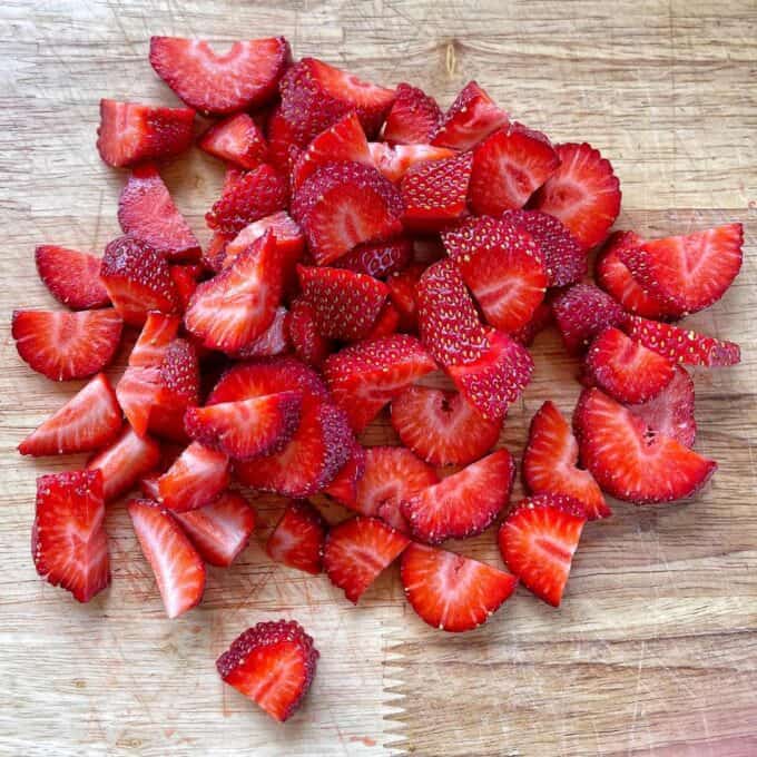 Sliced strawberries on a wooden chopping board.