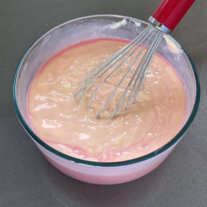 A glass bowl with custard and strawberry jelly being mixed through.