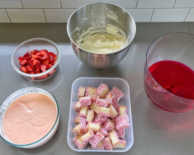 All of the sliced, whipped and set components to make Strawberry Lamingon Triffle on a grey bench top.