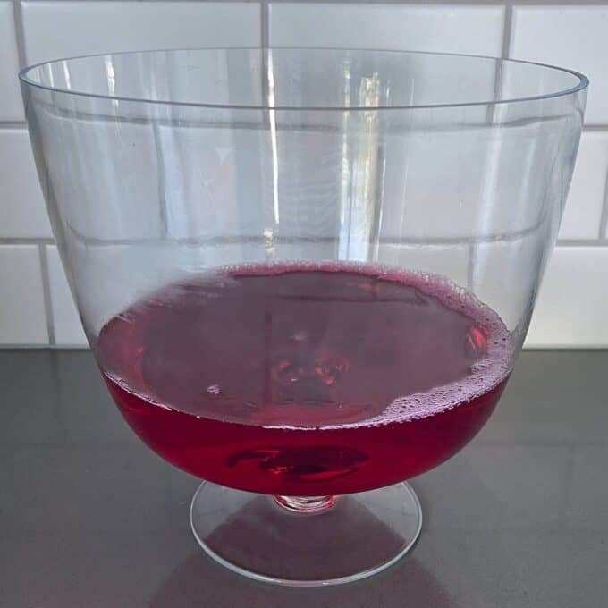 Strawberry jelly set in a glass triffle dish on a grey bench top.