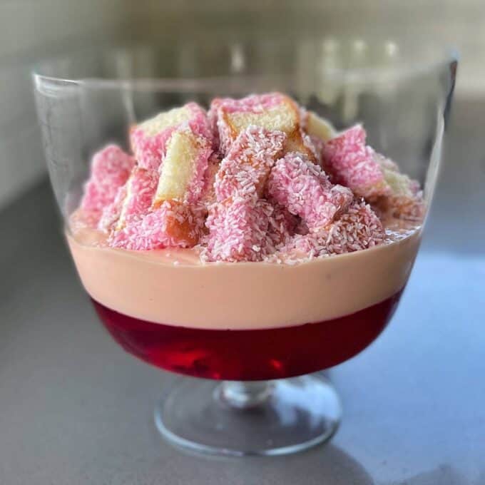 A half assembled strawbeery triffle. The jelly is on the bottom layer followed by strawberry custard and the sliced laningtons have been placed on top.