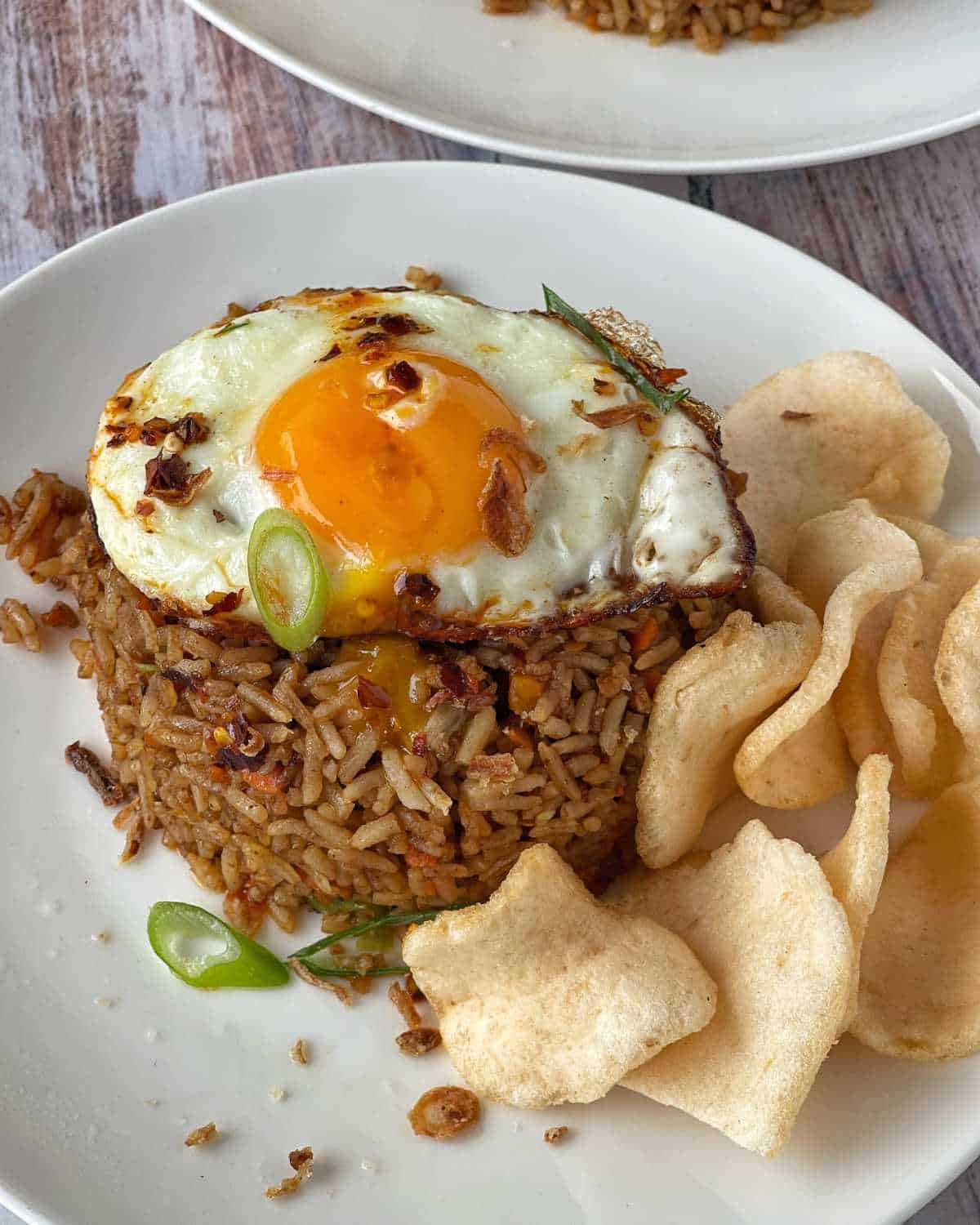Nasi Goreng served on a white dinner plate with a selection of prawn crackers and a fried egg.