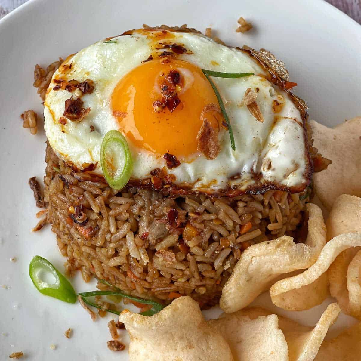 Nasi Goreng served on a white dinner plate with a selection of prawn crackers and a fried egg.
