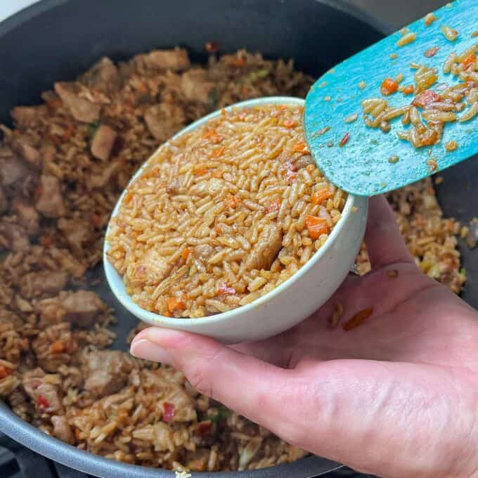 A small white bowl with Nasi Goreng being pushed inside it to serve upside down on a plate.