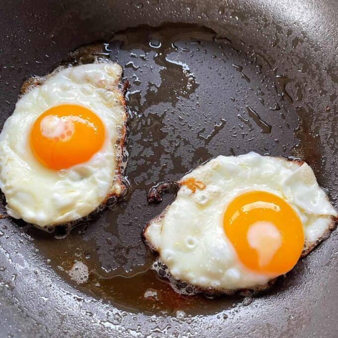 Two fried eggs frying in a frypan.