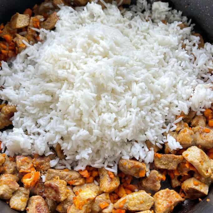 Cooked and cooled white rice being added to the Nasi Goreng mixture in a frypan.