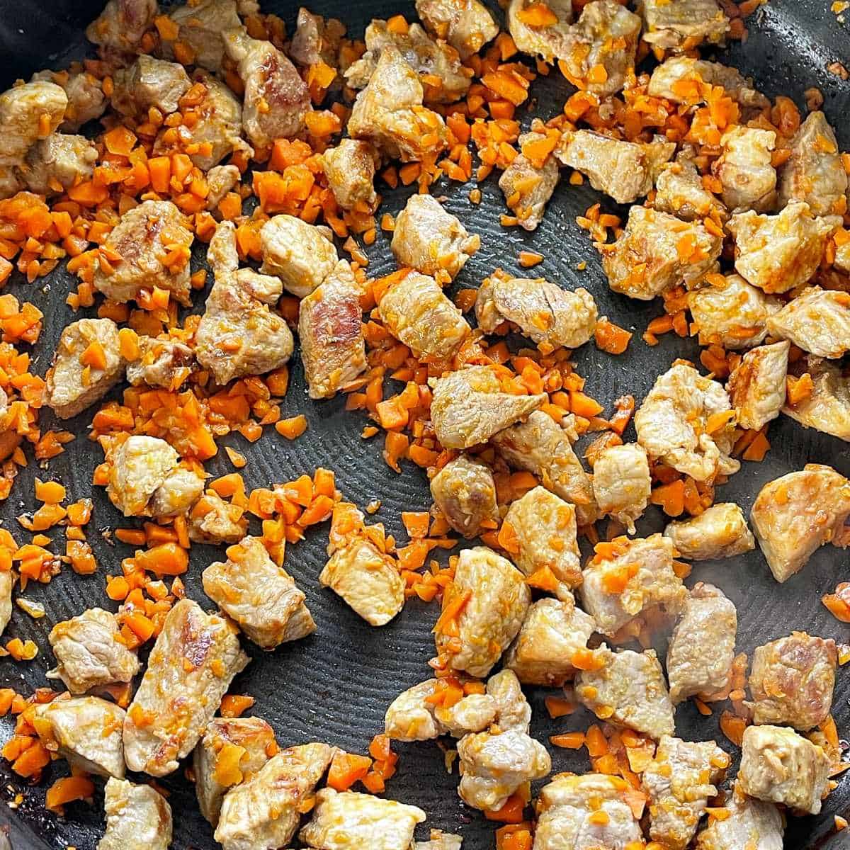 Cuded pork peices and diced carrot frying in a frypan.