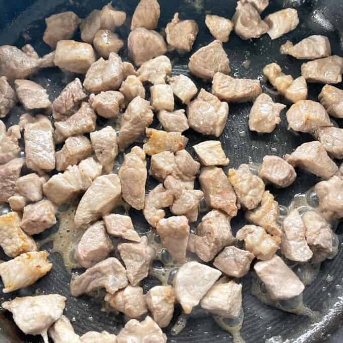 Cubed pork pieces frying in a frypan.