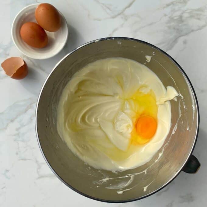 One egg being added to the cheesecake filling in a cake mixing bowl