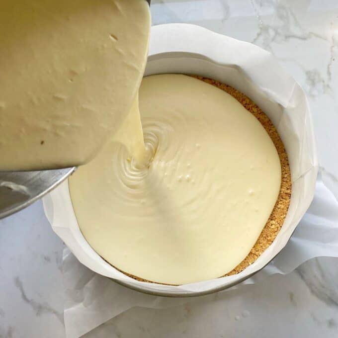 The cheesecake filling being poured into the round lined baking tin.