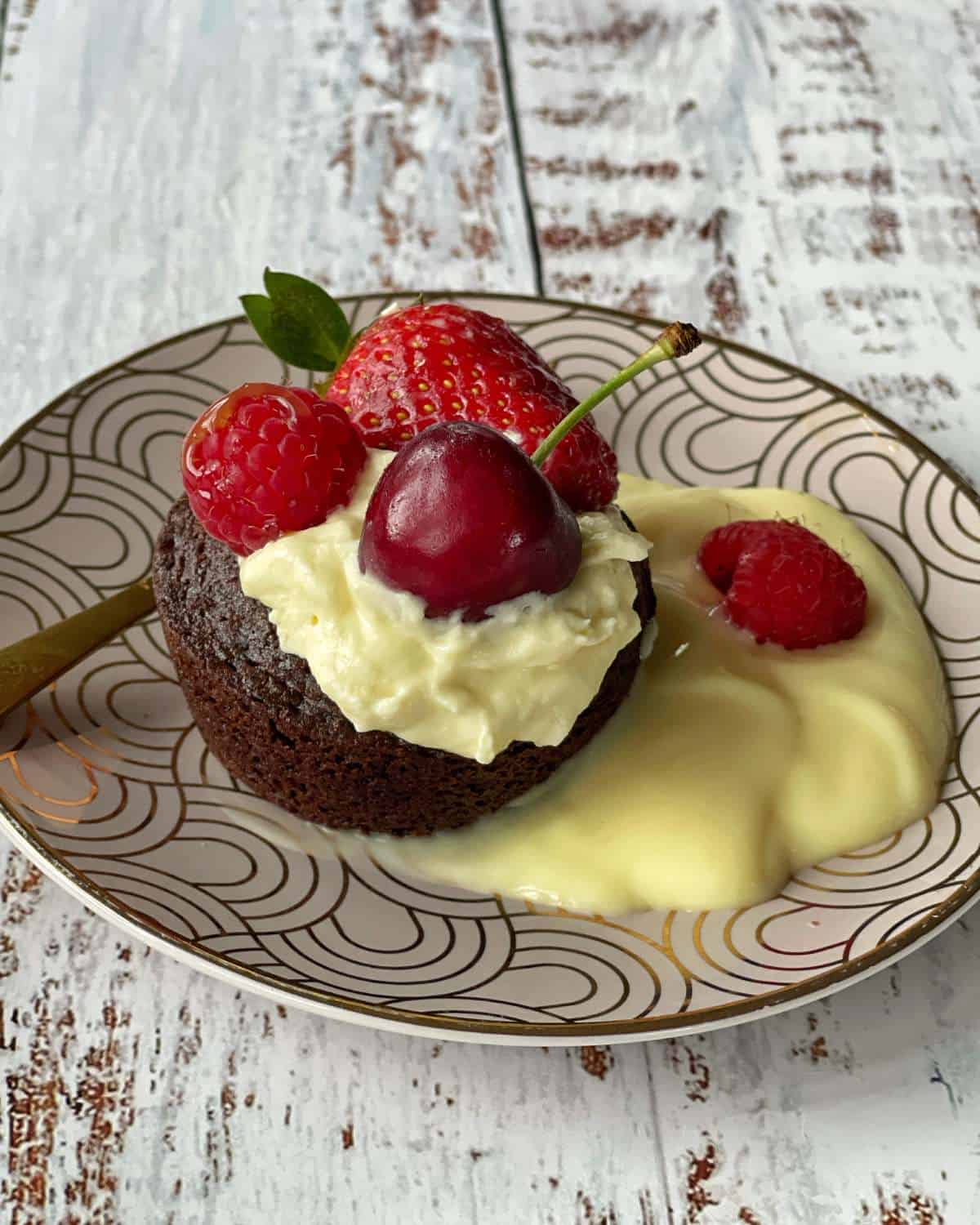 A close up of a piece of brownie with custard, cream and berries on a pink plate.