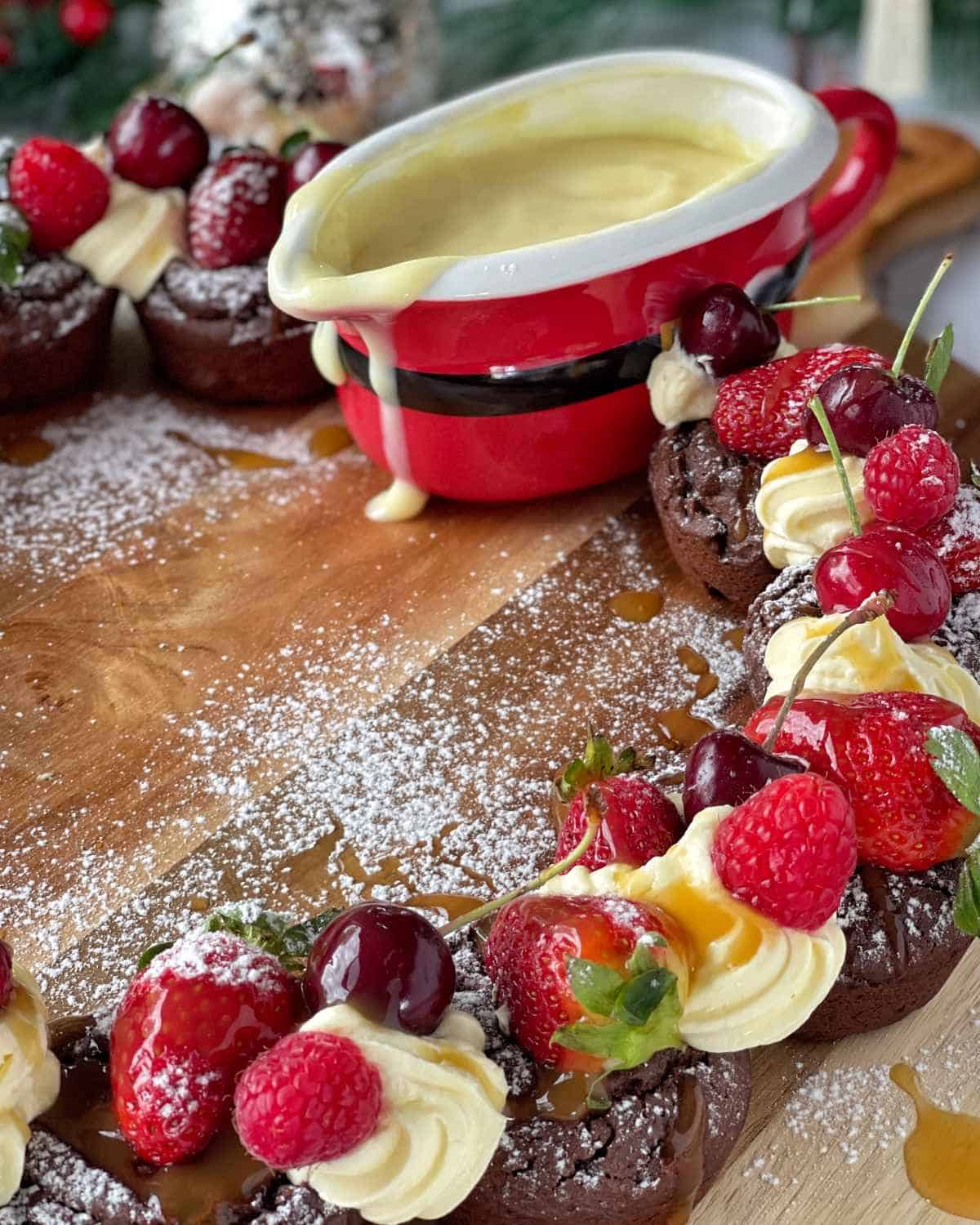A close up of a brownie wreath with custard on a wooden chopping board.