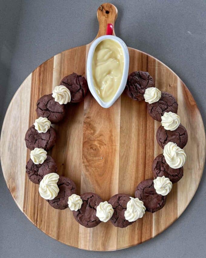 Brownies, cream and custard arranged in a circle on a circular chopping board.