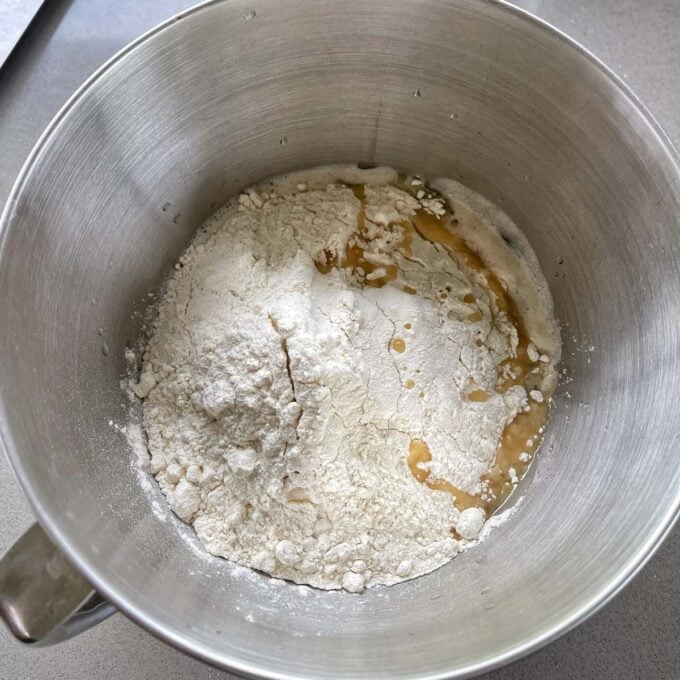 A stand mixer bowl with yeast and flour and honey in it.
