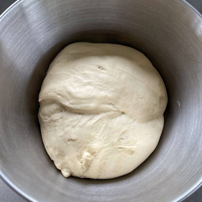Risen pizza dough in the base of a stand mixer.