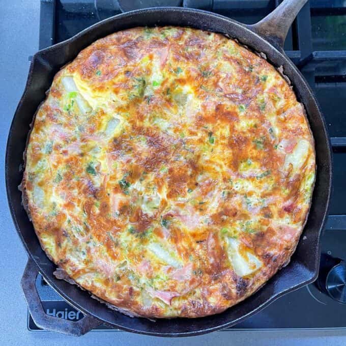 A cooked Ham and Potato Fritata in a round deep skillet frypan resting on the hob.