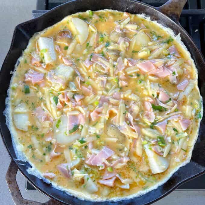 Ham and Potato Fritata cooking gently in a round deep dish skillet pan over a low to medium heat.