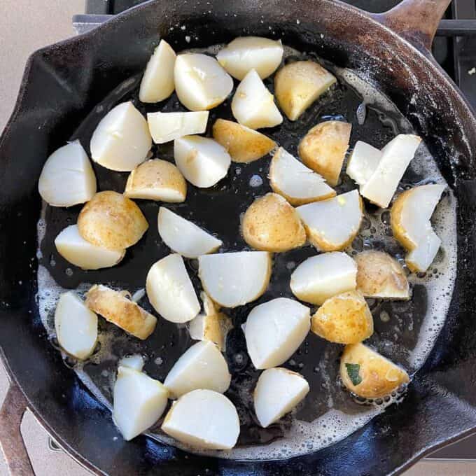 Cubed boiled potatoes frying in a round deep skillet pan in butter.