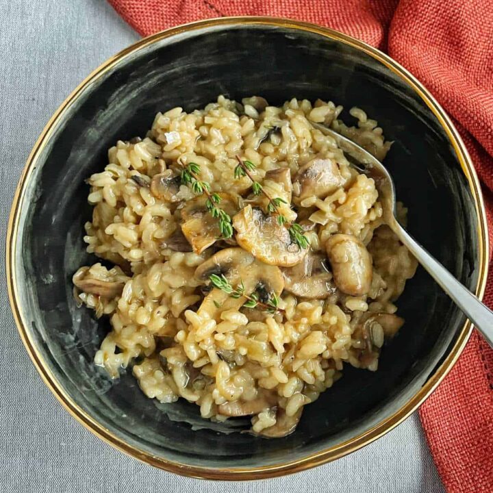 A small black bowl with a serving of Mushroom Risotto with three sprigs of thyme scattered on the top.