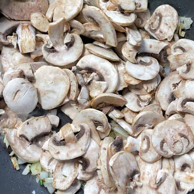 Sliced mushrooms being added to the sauteed onion and garlic mixture.