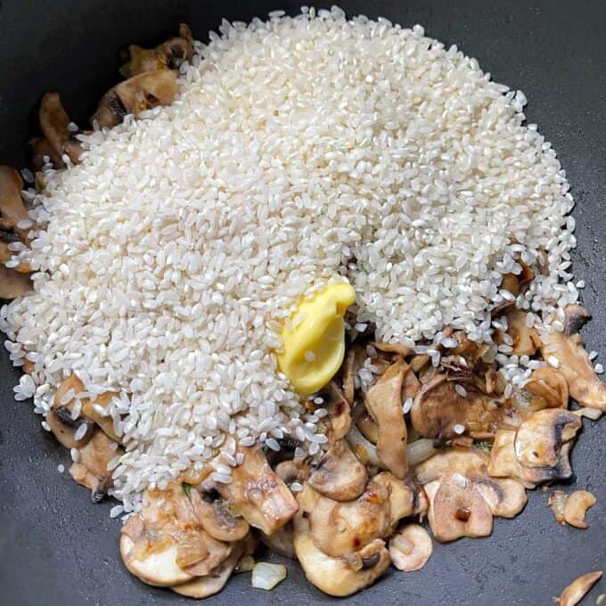 Risotto rice and butter being added to the mushroom and garlic mixture to make Mushroom Risotto in a frypan.