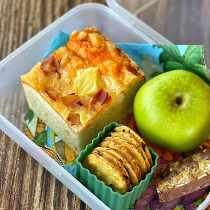 A piece of pizza bread sitting in a lunch box with other snacks.