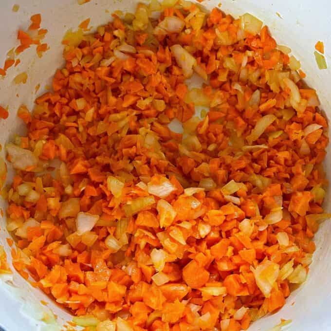 Cubed onion and carrot frying in a round ceramic dish over a medium heat