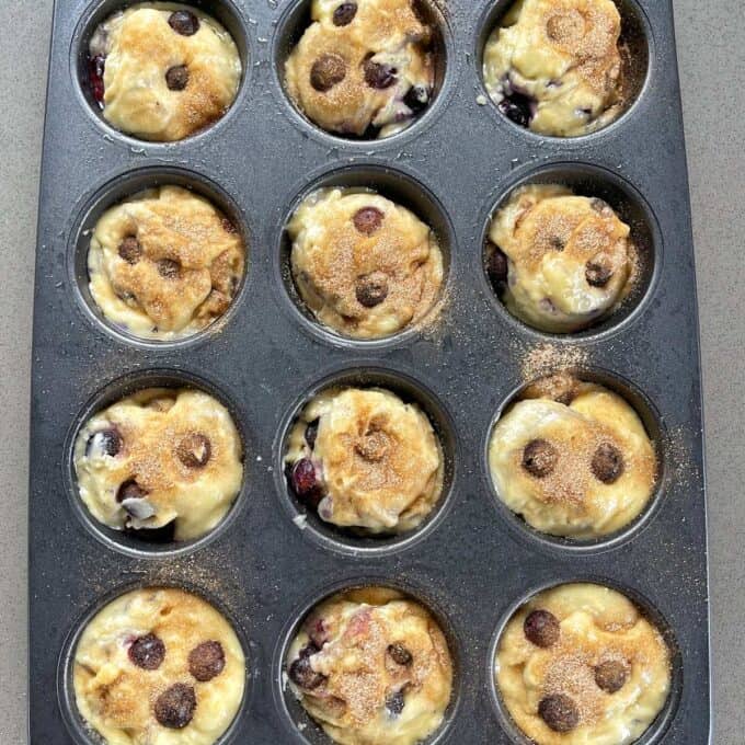 Blueberry muffin mixture in a muffin tin with a sprinkle of brown sugar dusted over the top.