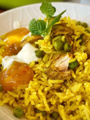 A white bowl of Chicken Biryani served with a small mint leave and a chutney.