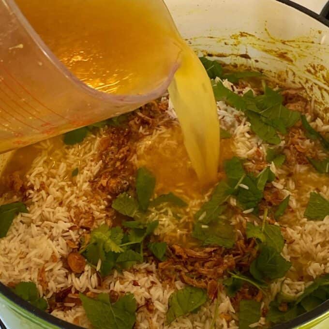Stock being poured into the Chicken Biryani mixture in a deep ceramic dish