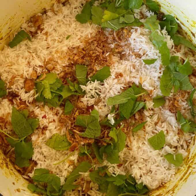 Herbs, spices and rice frying in a deep ceramic pot to make Chicken Biryani