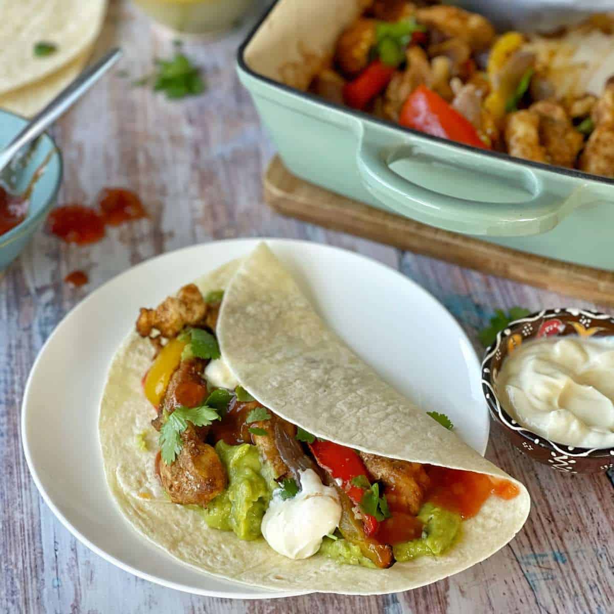 One Chicken Fajita served on a small white plate with a some coriander leaves and sourcream.