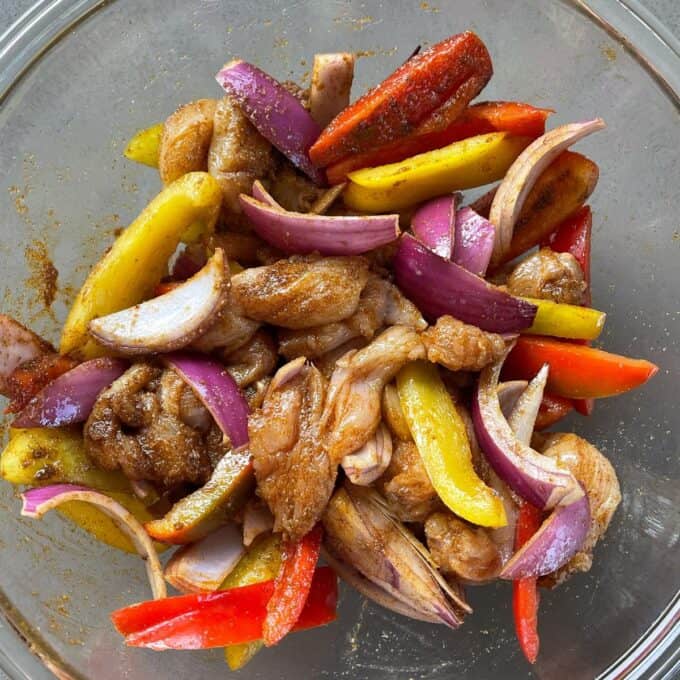 Marinated vegetables and chicken peices in a glass bowl.