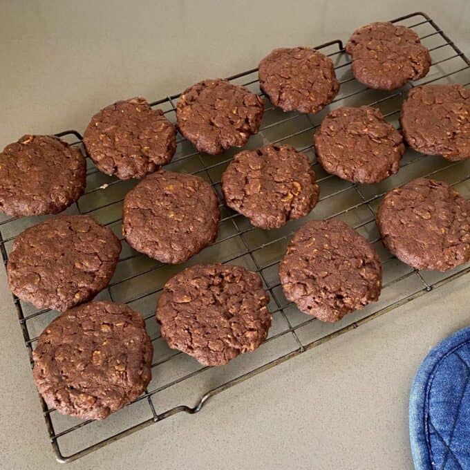 Cooked chocolate cornflake biscuits cooling on a wire rack on a grey bench top