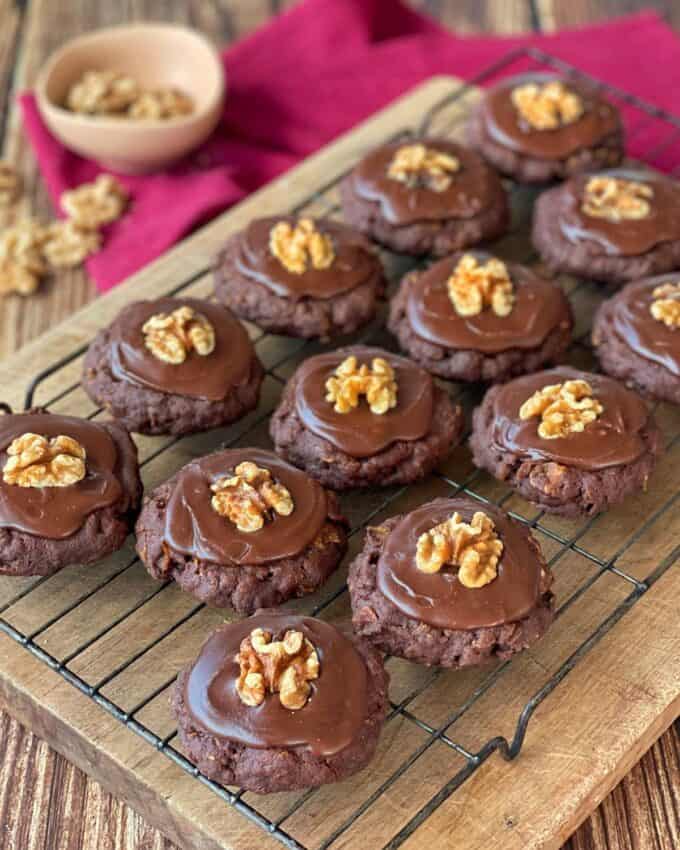 A selection of iced chocolate cornflake biscuits sitting on a cooling rack on a wooden chopping board.