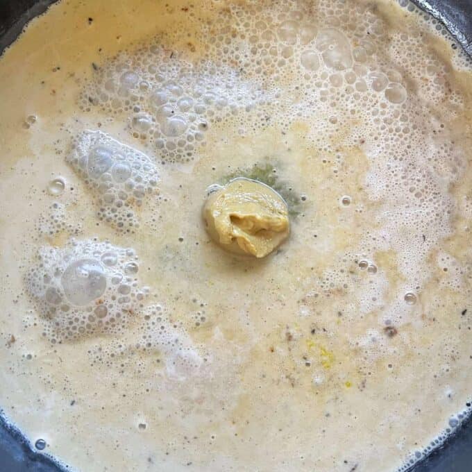 Dijon mustard being added to the creamy gravey in a frypan.