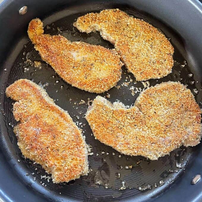 Four crumbed pork chops frying in a frypan