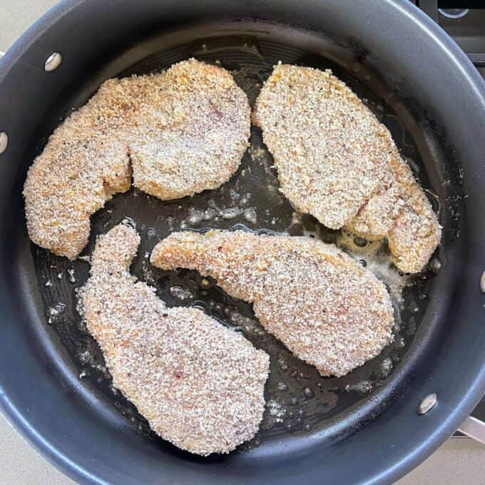 Four crumbed pork chops frying in a frypan