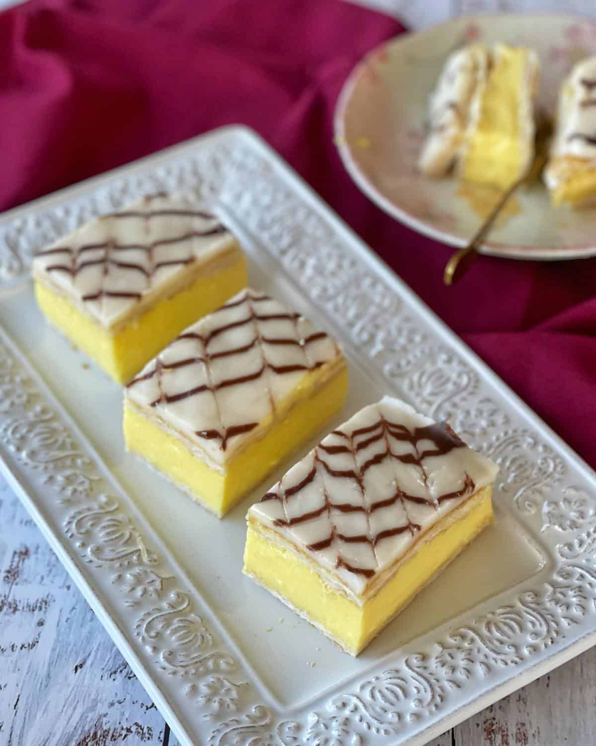 Three custard squares sitting on a white platter showing the different layers of filling.